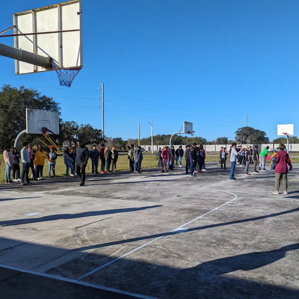 Estudiantes reuniéndose en una cancha de baloncesto al aire libre y soleada.