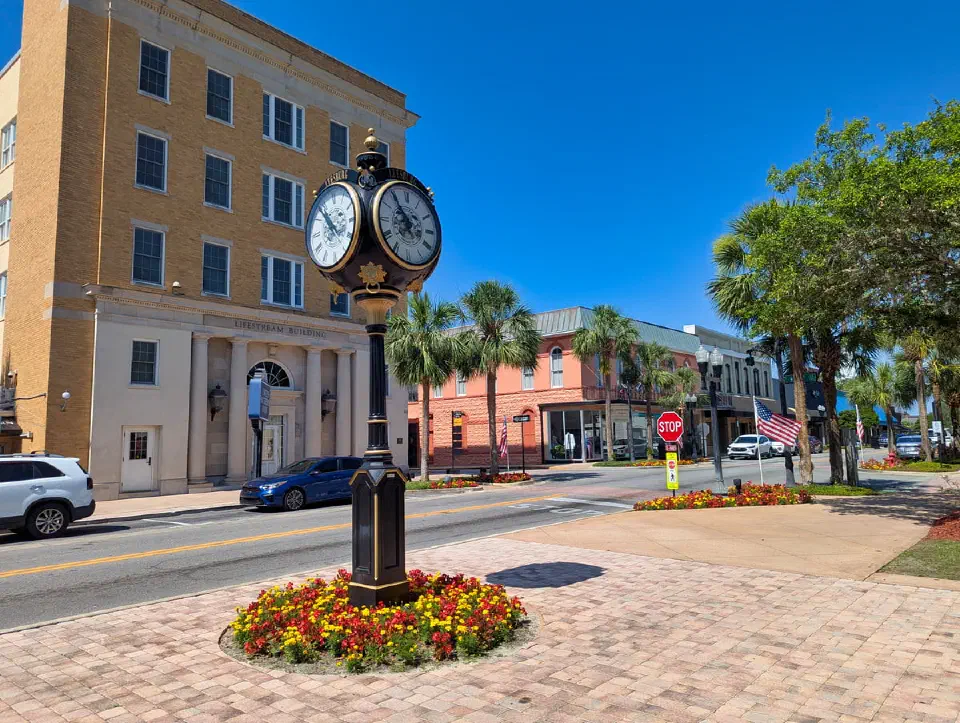 Centro de Leesburg con un reloj, edificios históricos y una bandera estadounidense bajo un cielo azul claro.