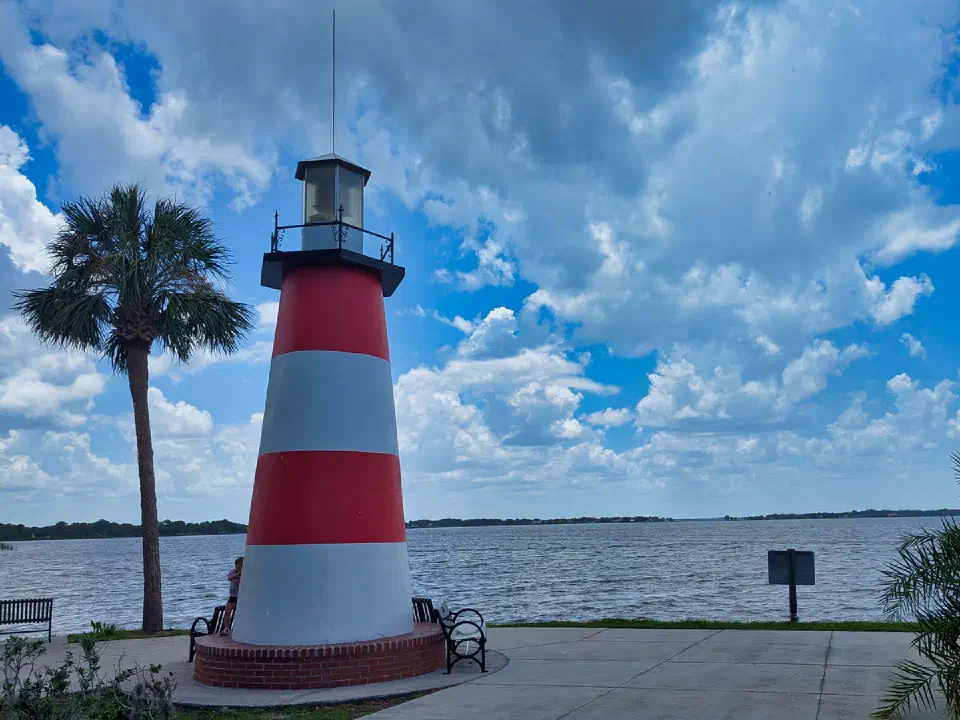 Faro de Mount Dora en Grantham Point con palmera, bancos y vistas al lago bajo un cielo nublado.
