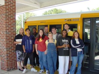Group of students in front of a yellow school bus.